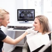 Konsultation hvor tandlægen viser røntgenbilleder til en patient ved skærmen.