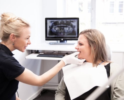 Konsultation hvor tandlægen viser røntgenbilleder til en patient ved skærmen.